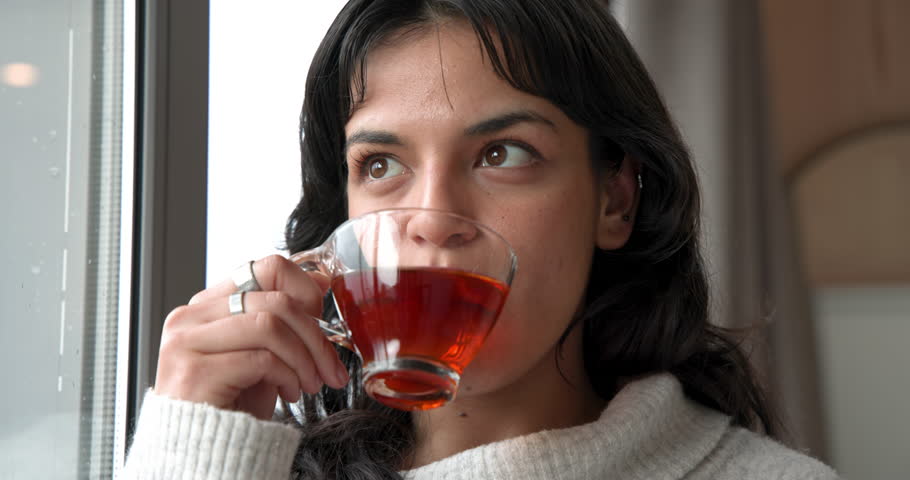 Woman enjoying warm tea in cozy sweater by window at home. relaxation, warmth, comfort, tranquility, lifestyle, beverage