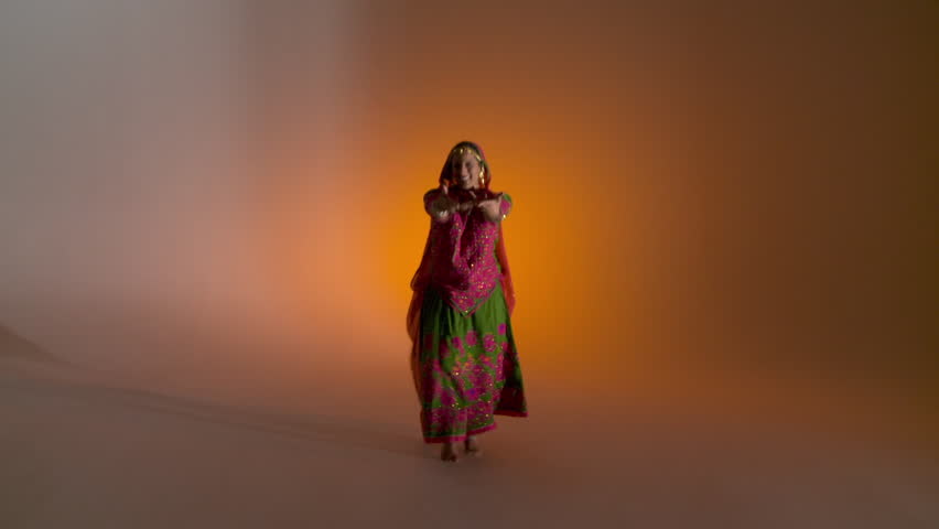 Indian girl in traditional folk costume dances against an orange colored