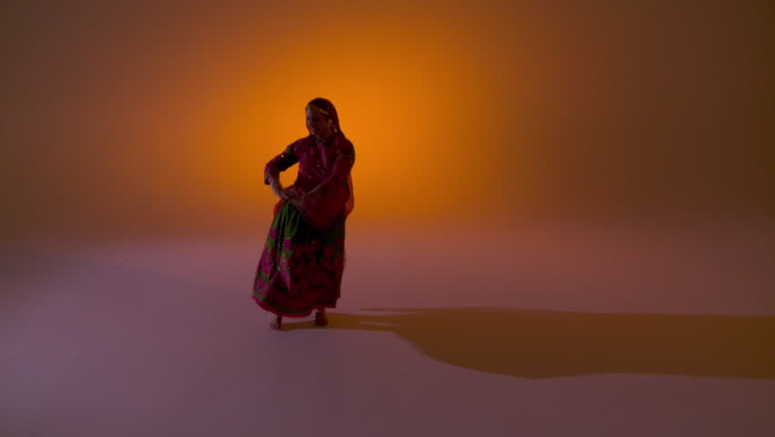 Indian girl in traditional folk dance costume spins as she dances against an