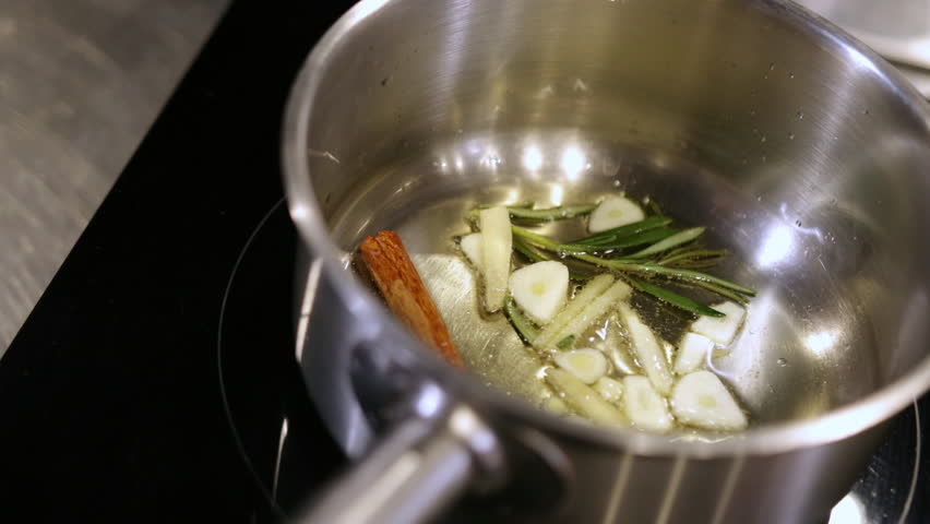Cinnamon stick, Garlic aroma, Fragrant cooking. In stainless steel pan, garlic slices, sprigs rosemary, and cinnamon stick are being cooked in oil.
