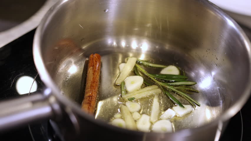Cinnamon stick, Garlic aroma, Fragrant cooking. In stainless steel pan, garlic slices, sprigs rosemary, and cinnamon stick are being cooked in oil.