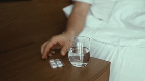Closeup of young Caucasian man sitting on bed with glass of water, taking sleeping pills or painkillers at home. Unrecognizable millennial male using medications, holding tablet in hand, selective - Powered by Shutterstock - Get 15% off with code: PIKWIZARD15
