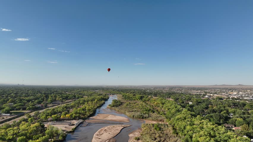 Drone POV of hot air balloons flying over stream in Albuquerque, New Mexico with clear blue skies.