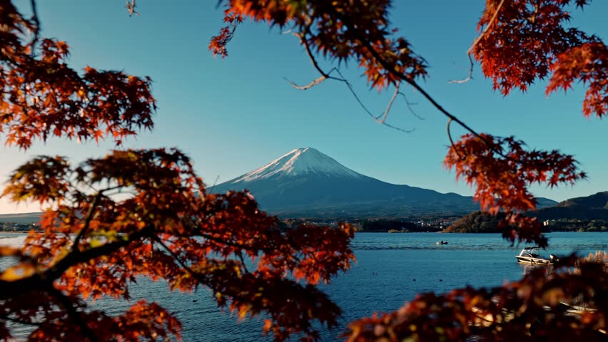 A breathtaking view of Mount Fuji reflected in the calm waters of Lake Kawaguchiko, surrounded by vivid red autumn foliage.
