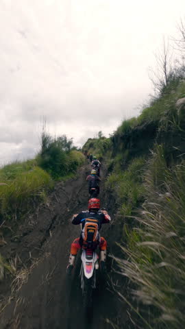 Vertical video 4k. Extreme moto enduro riders group speed race on mountain ridge dirt path at volcano hilly valley aerial view. FPV drone shot motorcycle motocross bike people riding rocky terrain