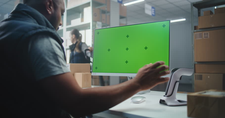 Delivery Service: African American Warehouse Associate Scans Code on Cardboard Box with Scanner, Enters Parcel Information on Computer. PC Screen Shows Green Screen Chroma Key Mock Up. Handheld.
