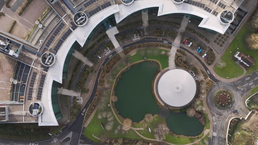 Top-down aerial fly-out showcasing a modern office complex with solar-panel rooftops, accentuating water features, green landscaping, and sleek curved architecture