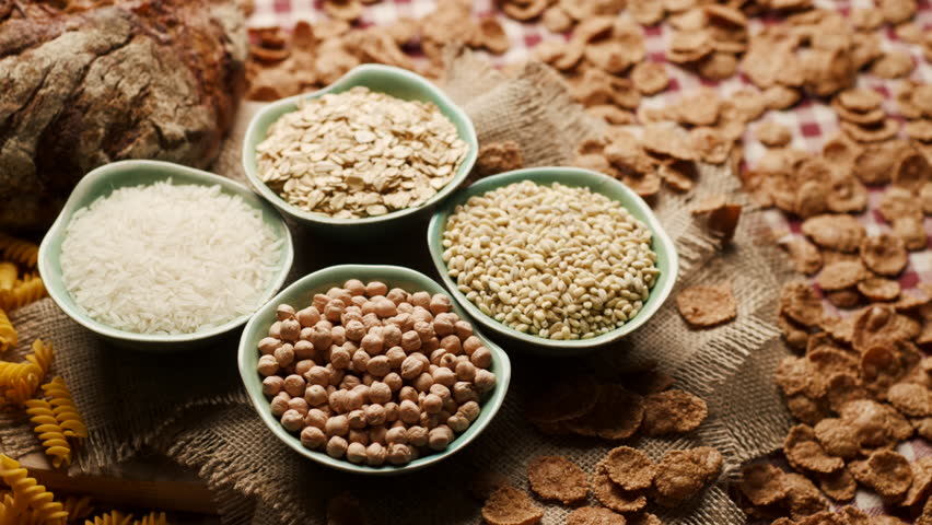 Close-up of carbohydrate-rich foods on a table, including bread, rice, wholegrain flakes, oats, wheat and corn pasta. Carbs Food.