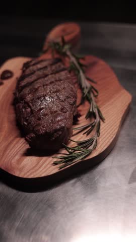 A slow-motion vertical footage of stamping a fresh grilled steak with branding iron stamp, on a rustic background