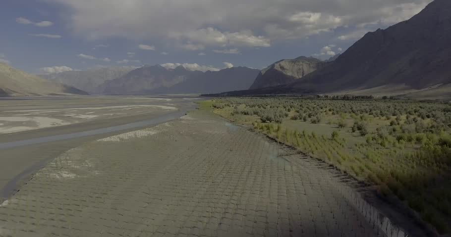 Aerial view of the majestic Indus River winding through a scenic valley surrounded by rugged mountains under a serene sky, Gilgit Baltistan, Pakistan.