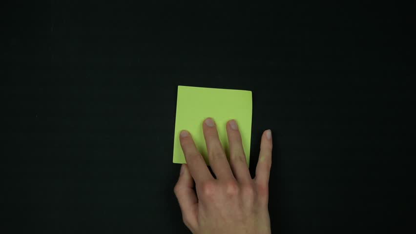 A fragile woman's hand sticks a yellow paper note on black background