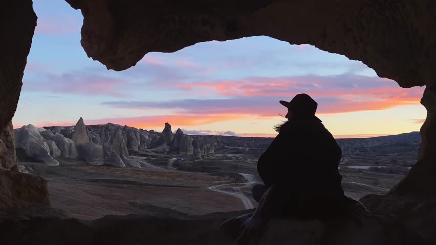 Silhouette woman sit cave on geological formations of Cappadocia watch wonderful sunset sky with fairy chimney panorama. Goreme travel destination. Turkey holiday destination. Unesco world heritage