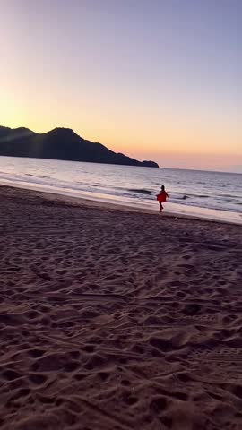 A woman runs along a Costa Rican beach at sunset, as the waves crash and the sky glows in warm hues.