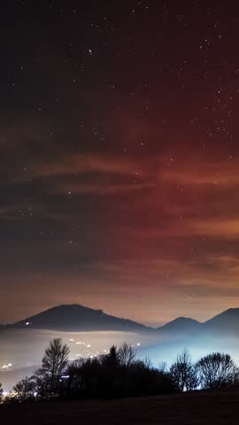 vertical video,Red Aurora Borealis Over Carpathian Hills Night Sky with Gentle Fog in a Rural Valley Landscape