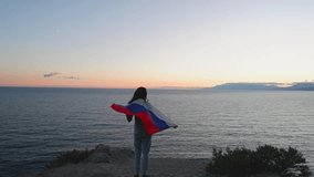 A brunette woman with a Russian flag on her shoulders stands on a rocky seashore at sunset. Gives independence, patriotic holiday concept. - Powered by Shutterstock - Get 15% off with code: PIKWIZARD15