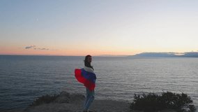 A brunette woman with a Russian flag on her shoulders stands on a rocky seashore at sunset. Gives independence, patriotic holiday concept. - Powered by Shutterstock - Get 15% off with code: PIKWIZARD15