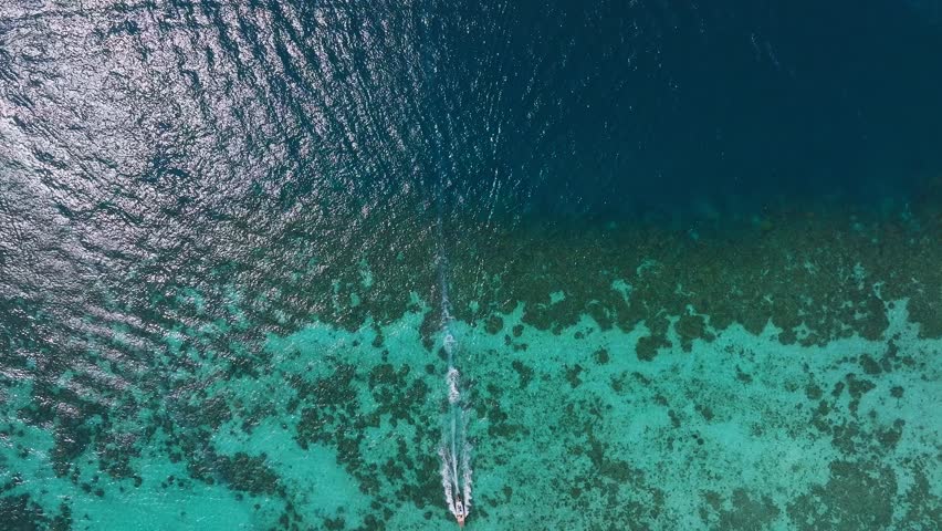 Aerial view of Phi Phi Island's turquoise waters with speedboats gliding, leaving white trails, and coral reefs visible beneath the clear sea.