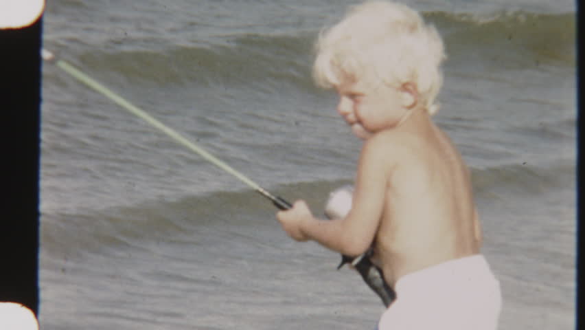 Vintage shot of a focused child reeling in his fishing rod, standing against the backdrop of rolling ocean waves