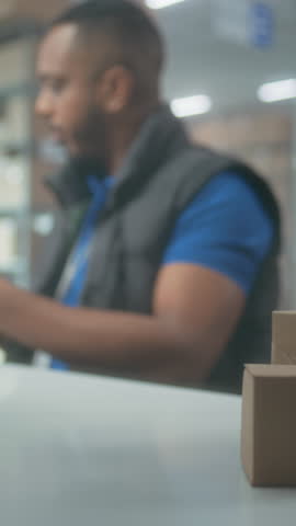 African American warehouse clerk scans parcels using tablet computer, works in post office. Sorting center employees carrying cardboard boxes for shipping. Logistics storage with online store products