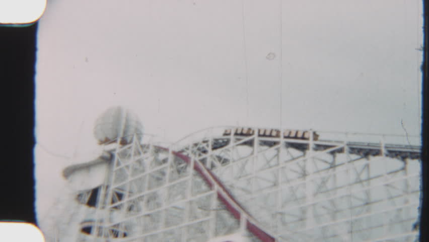 Vintage footage of a classic amusement park roller coaster, captured on analog film against a bright sky
