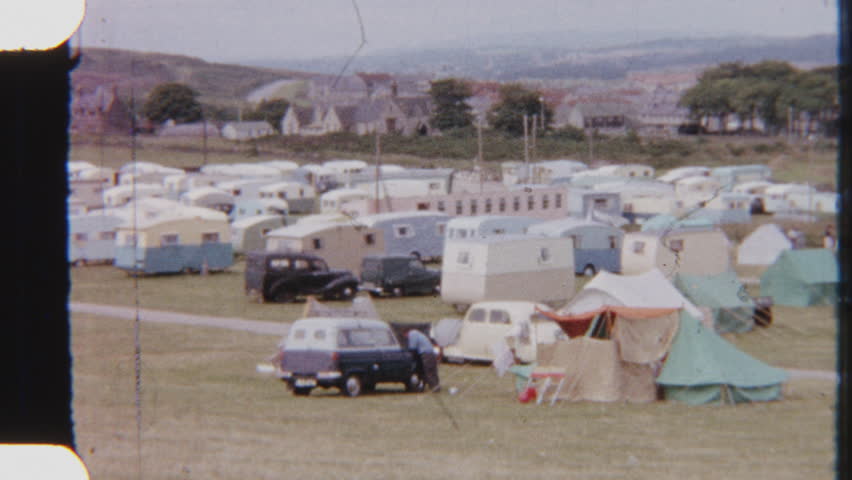 Captured on 8mm film, a nostalgic sunny day at the campsite featuring vintage cars and mobile homes, set against a tranquil outdoor backdrop