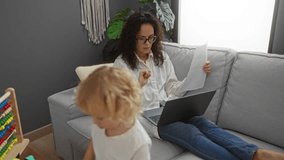 Woman working from home on a laptop while holding documents in a cozy living room with child playing nearby, showcasing remote work and family life balance indoors. - Powered by Shutterstock - Get 15% off with code: PIKWIZARD15