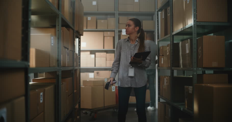 Female Warehouse Associate Scans Cardboard Boxes with E-Commerce Online Orders on Shelves Using Scanner, Checks Delivery Information of Packages on Tablet Computer. Sorting Center of E-Commerce Store.