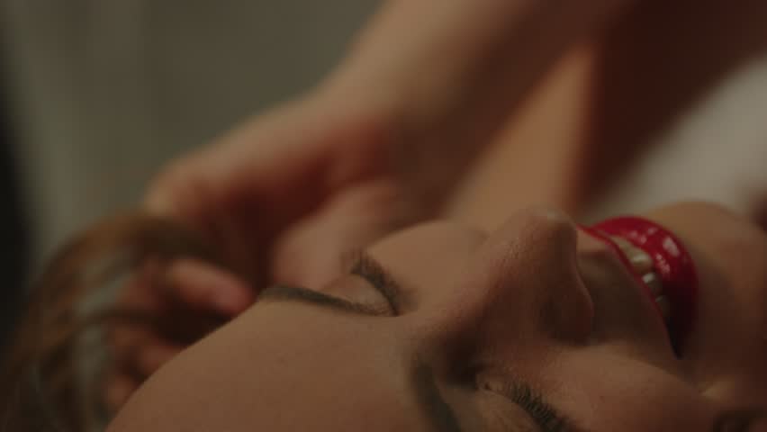 Macro of A beautiful girl wearing bright red lipstick sensually playing with her hair and looking at the camera
