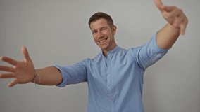 Man smiling joyfully on white background wearing blue shirt with open arms showcasing happiness in a portrait style image with an isolated minimalistic setting. - Powered by Shutterstock - Get 15% off with code: PIKWIZARD15