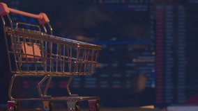Modern economics. Business concept of securities trading. A small shopping cart from a supermarket stands against the background of a computer monitor on which economic data is changing. Close-up. - Powered by Shutterstock - Get 15% off with code: PIKWIZARD15