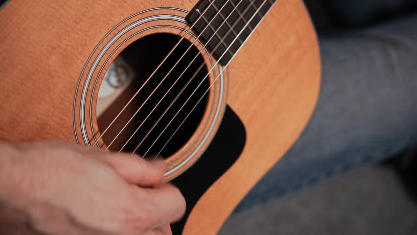Man playing acoustic guitar. Close-up, guitar deck and musician's hand. Wooden