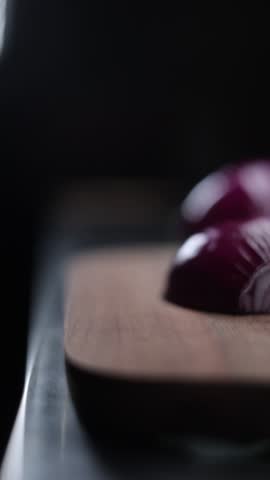 A vertical closeup slow-motion of slicing onion with a kitchen knife on the wooden cutting board