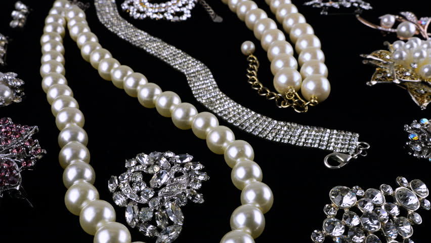 Vintage costume jewelry, brooches and necklaces, with crystals and imitation pearls on a rotating black velvet display case.