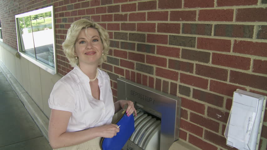Woman walks up, opens night deposit box at bank, turns to the camera and smiles