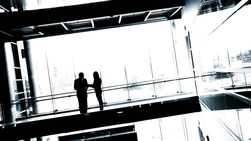 Silhouetted businessman and woman meet against a backdrop of white windows. High