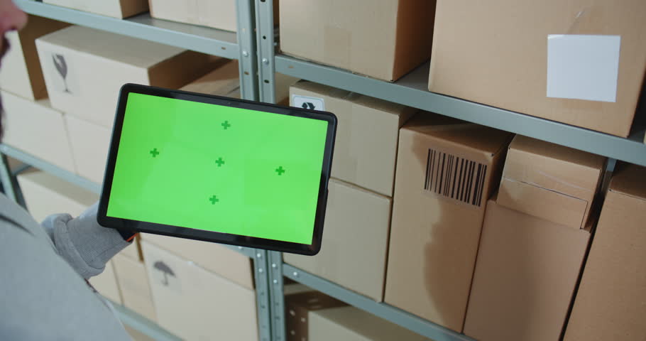 Postal Warehouse Worker Scans Code on Cardboard Box with Barcode Scanner, Checks Package Information, Monitors Parcel Delivery Route. Tablet Computer Display Shows Green Screen Chroma Key. Close Up.