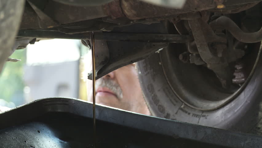 Auto mechanic drains off the oil from an old car. Detail shot with mechanic