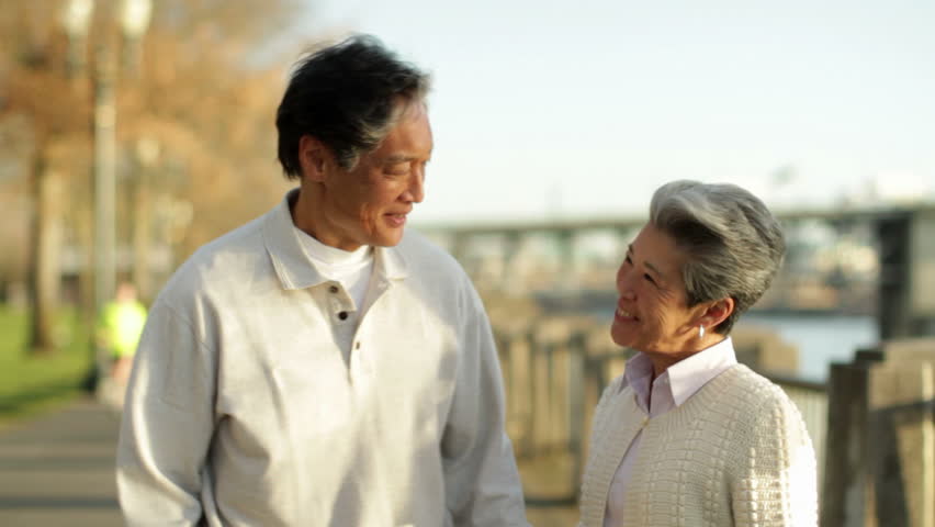 Older asian couple standing, talking in a park beside the Willamette River in