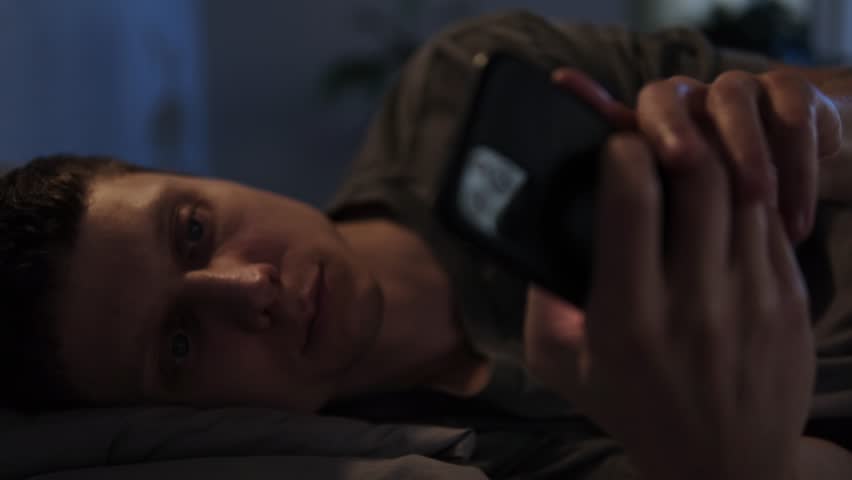 Man lying in bed late at night, glued to his phone, unable to sleep due to overstimulation from digital content and social media.