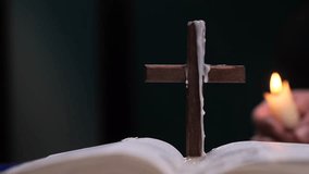 Wooden cross with candle wax drippings on open bible with lit candle in background - Powered by Shutterstock - Get 15% off with code: PIKWIZARD15