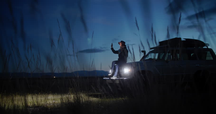 Young woman sitting in her car surrounded by nature at night, using her smartphone to photographing while embracing the peace and tranquility of the serene landscape