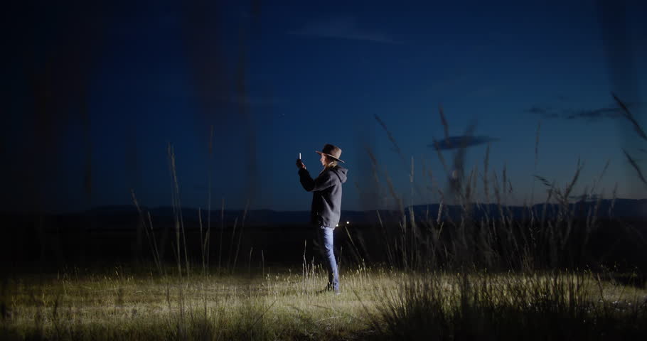 Young woman sitting in her car surrounded by nature at night, using her smartphone to photographing while embracing the peace and tranquility of the serene landscape