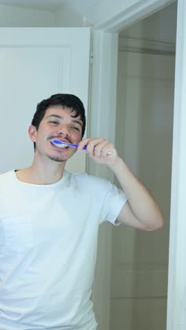 Vertical video of man just woke up, brushing his teeth in front of the bathroom mirror, personal hygiene