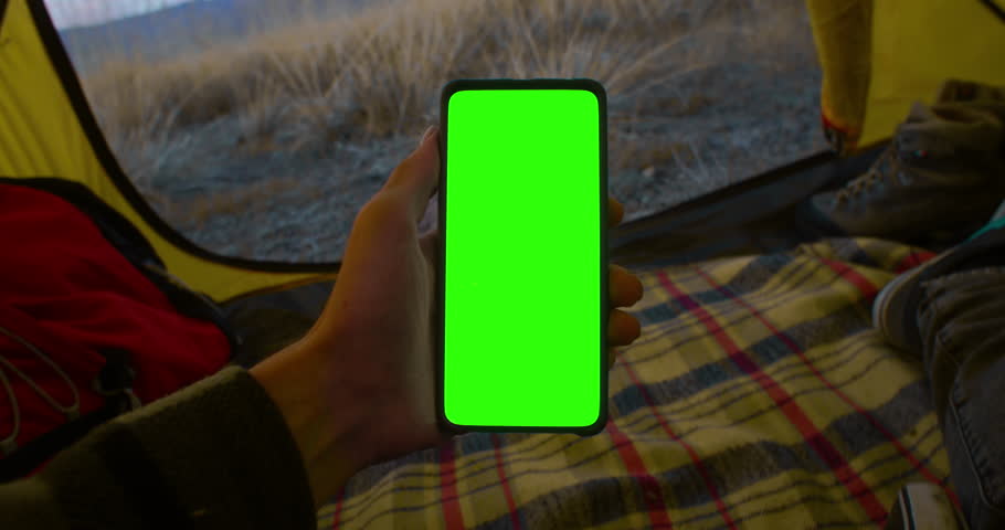 POV person is comfortably relaxing inside a tent while using a smartphone and enjoying the beauty of the great outdoors