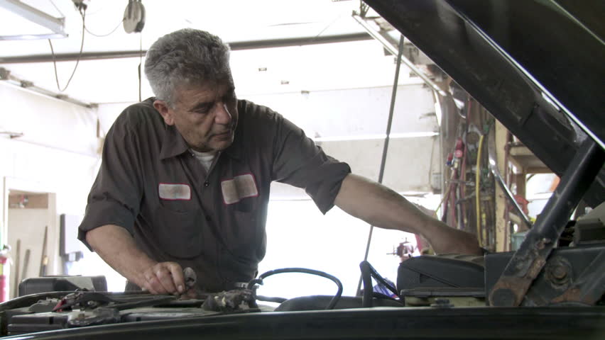 Auto mechanic checks the oil in a car engine. Hand held camera with strong