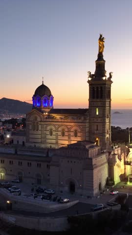 vertical view: aerial shot of Marseille cathedral at night illuminated, drone view of Notre Dame de la Garde in France, travel in French Riviera. 