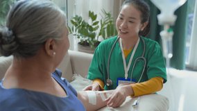 Tilt down shot of cheerful Asian young female caregiver setting intravenous line for relaxed elderly woman while visiting her at home - Powered by Shutterstock - Get 15% off with code: PIKWIZARD15
