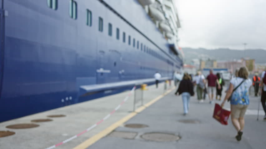 Blurred scene of people walking alongside a cruise ship at an outdoor port, showcasing a casual, vacation atmosphere with men and women leisurely strolling on the dock.