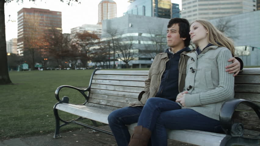 Attractive young couple sitting on a bench, talking and laughing with the city