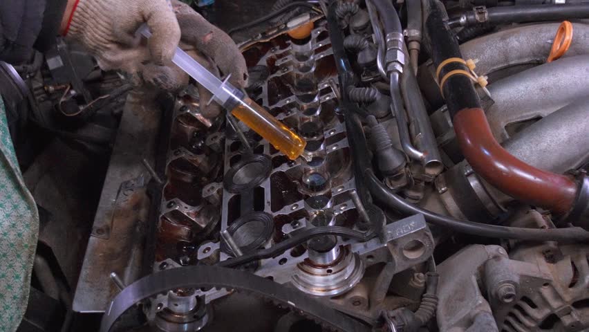 Mechanic in gloves pours engine oil on camshaft bed of car engine with syringe. In this process, main methods of maintenance and repair in car garage are highlighted